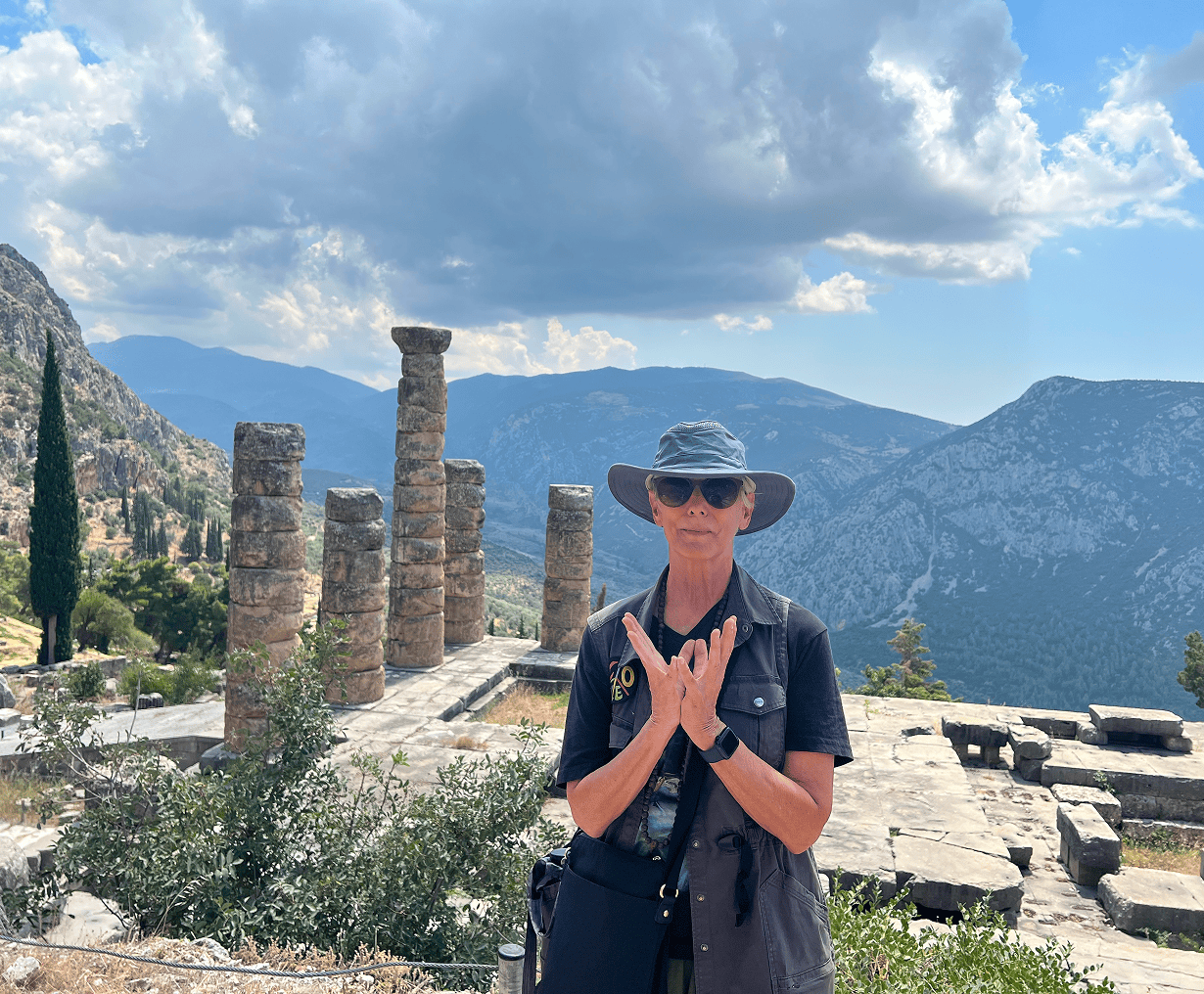 Person posing at ancient ruins, mountainous backdrop.